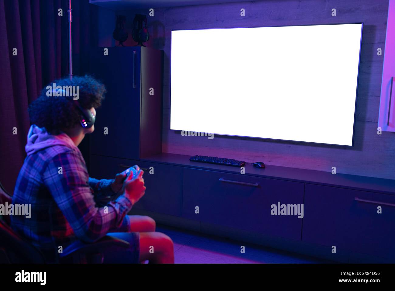 Un giovane maschio birazziale che gioca ai videogiochi a casa, siede in una stanza buia, copia spazio Foto Stock