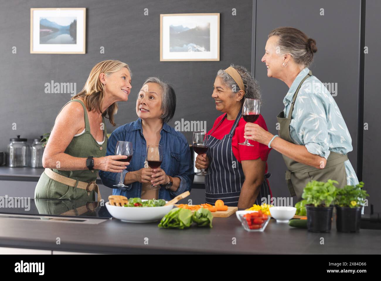 Diverse amiche anziane si godono il vino a casa in un'accogliente cucina Foto Stock