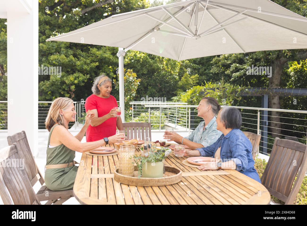 Diverse amiche anziane che si godono un pasto all'aperto, una sola in piedi Foto Stock