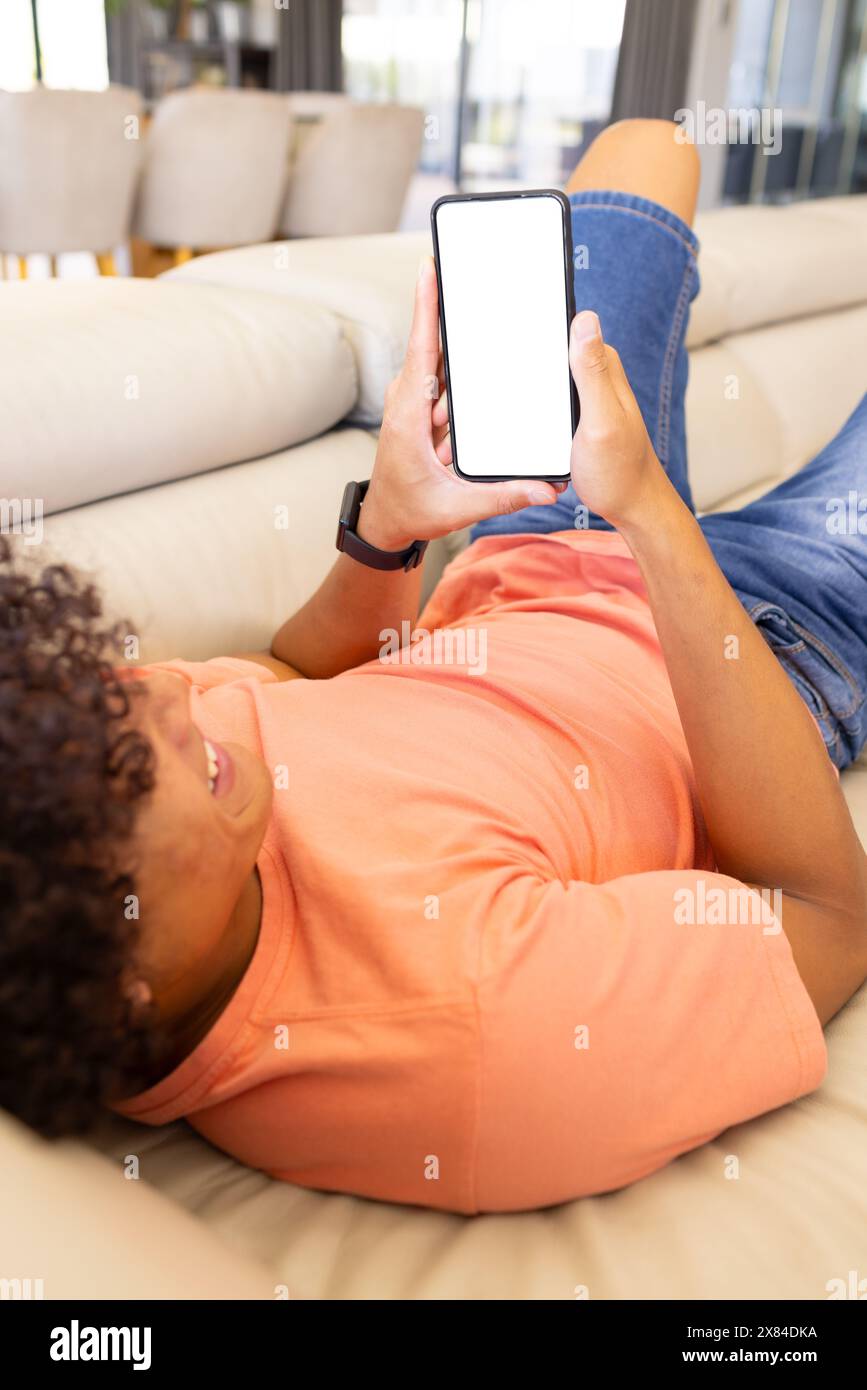 Un giovane uomo birazziale che si rilassa a casa, tiene in mano lo smartphone, copia lo spazio Foto Stock