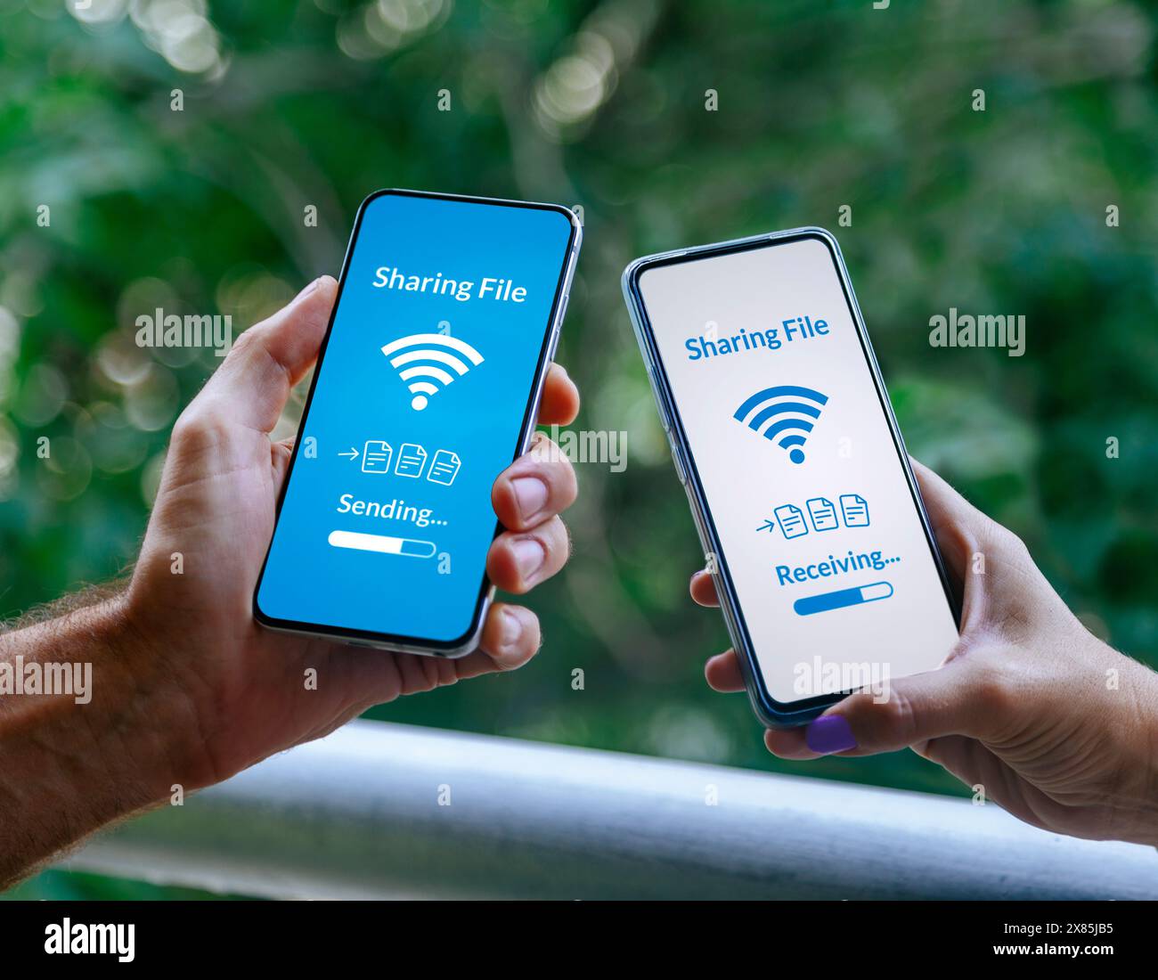 Mani di due persone con telefoni cellulari che condividono file tramite tecnologia wireless. Invio e ricezione di informazioni tramite smartphone. Foto Stock