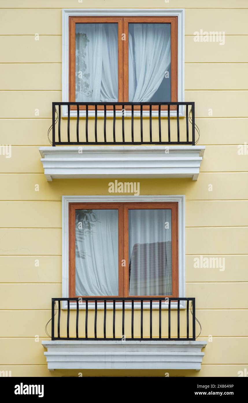 Due finestre moderne con tende su parete gialla, vista esterna. Finestra di fronte all'esterno di una casa moderna. Architettura esterna. Bella colorata Foto Stock