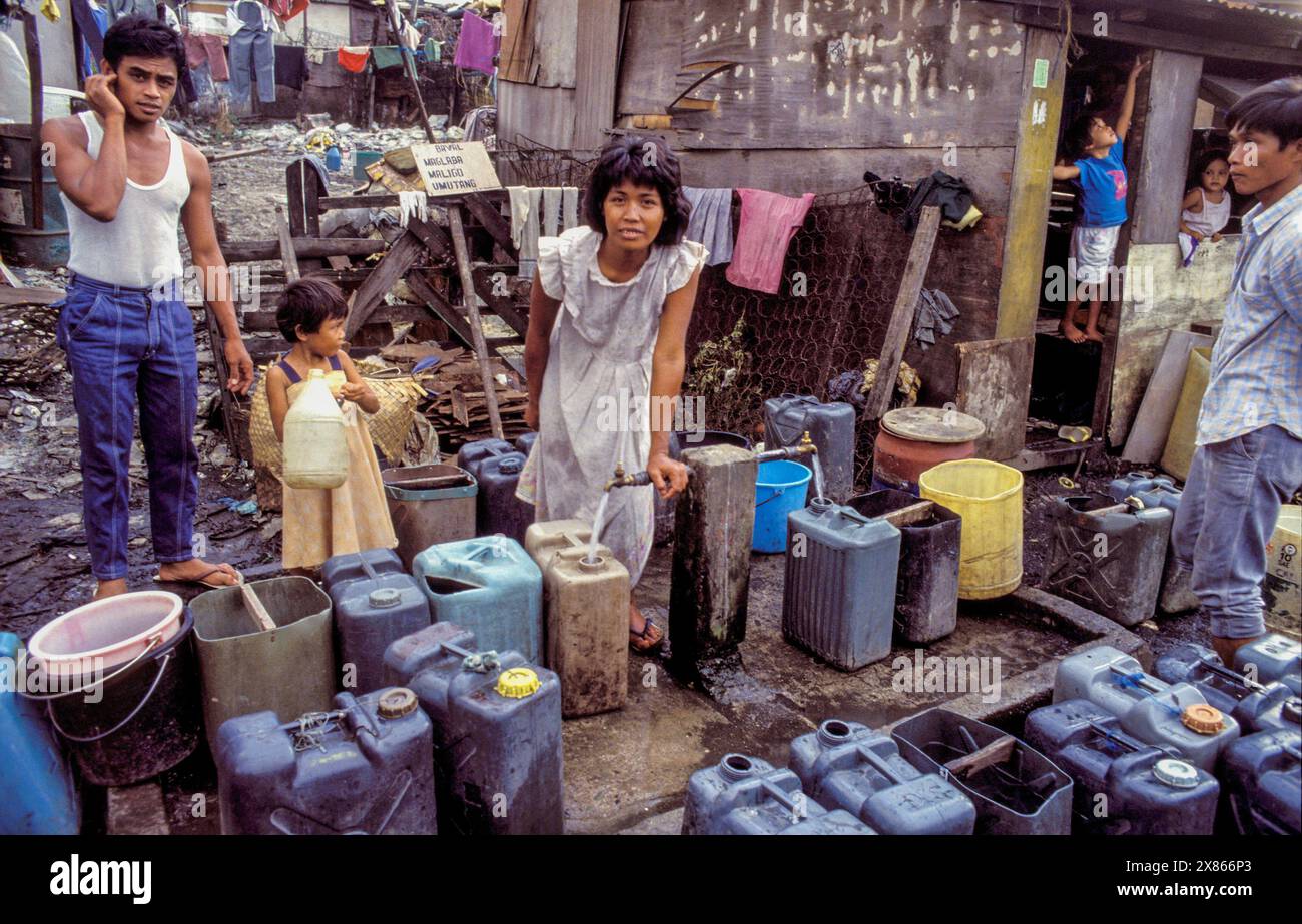 Filippine, Manila; Una madre riempie i jerrycan di acqua potabile in una baraccopoli. Foto Stock