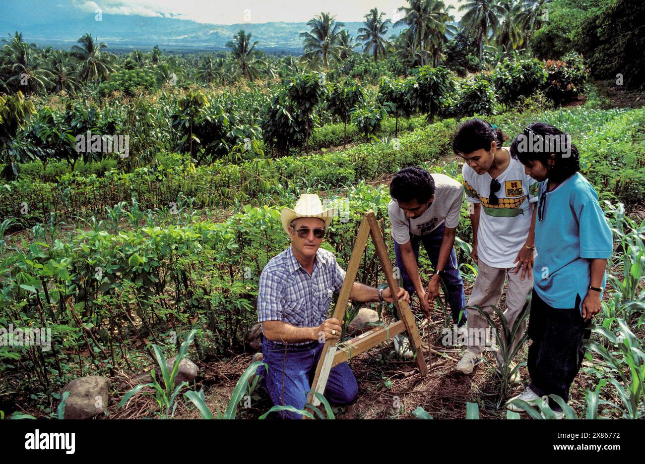 Filippine, Mindanao; operaio dello sviluppo e agricoltori locali che misurano il livello di un campo collinare dove le colture crescono su terrazze che prevengono le malattie Foto Stock