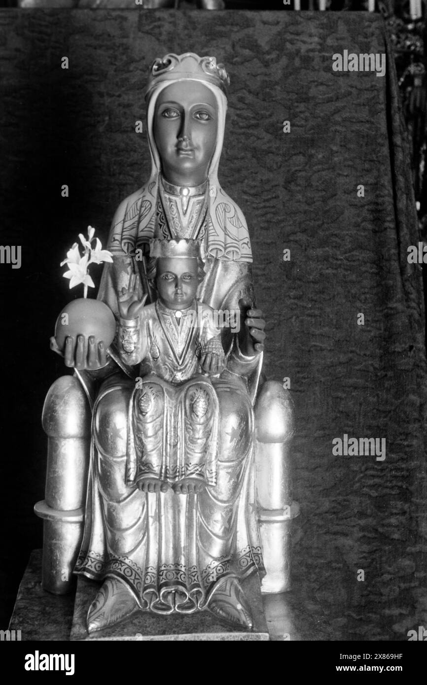 Madonnenstatuette mit Jesuskind im romanischen Stil, vermutlich modelliert nach der Schwarzen Madonna von Montserrat, von der sie sich in Details der Bemalung und den Gesichtszügen unterscheidet, zusätzlich wurde die Kugel des Universums, die sie in der rechten hand hält mit einem Zweig Weißer Lilien, Sympol für Reinheit, kombiniert, Barcellona 1957. Statuetta della Madonna col bambino in stile romanico, probabilmente modellata sulla Madonna Nera di Montserrat, da cui si differenzia per i dettagli del dipinto e delle caratteristiche facciali; inoltre, la sfera dell'universo, che detiene Foto Stock