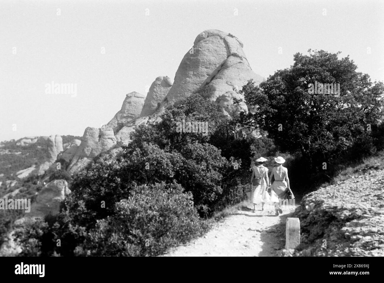 Zwei Frauen wandern auf dem Bergmassiv Montserrat, vor ihnen liegen die Gipfel Gorra Frígia, Magdalenes und Gorra Marinera, Katalonien 1957. Due donne che camminano sul massiccio del Montserrat, con le vette di Gorra Frígia, Magdalenes e Gorra Marinera di fronte a loro, Catalogna 1957. Foto Stock