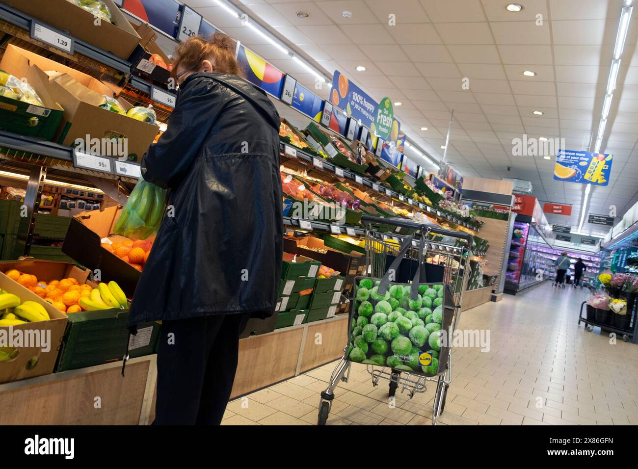Dietro dietro la vista di una donna anziana che acquista frutta e verdura nel negozio interno della borsa del carrello del supermercato Lidl UK 2024 KATHY DEWITT Foto Stock