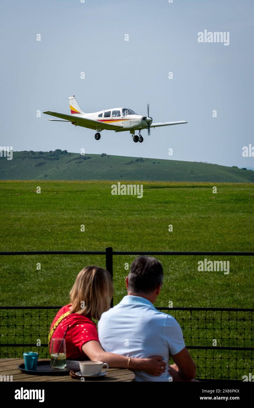 Un uomo e una donna guardano un aereo leggero Piper Warrior atterrando all'aeroporto di Compton Abbas nel Dorset, in Inghilterra Foto Stock