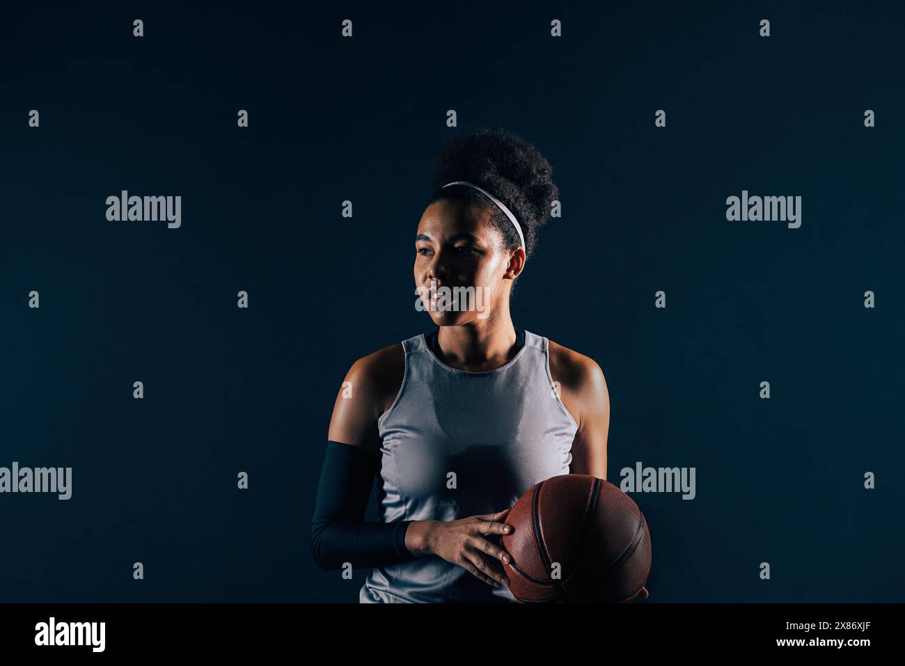 Giocatrice di basket femminile in abbigliamento sportivo su sfondo nero. Giovane giocatore professionista di basket con palla, con abbigliamento da squadra. Foto Stock
