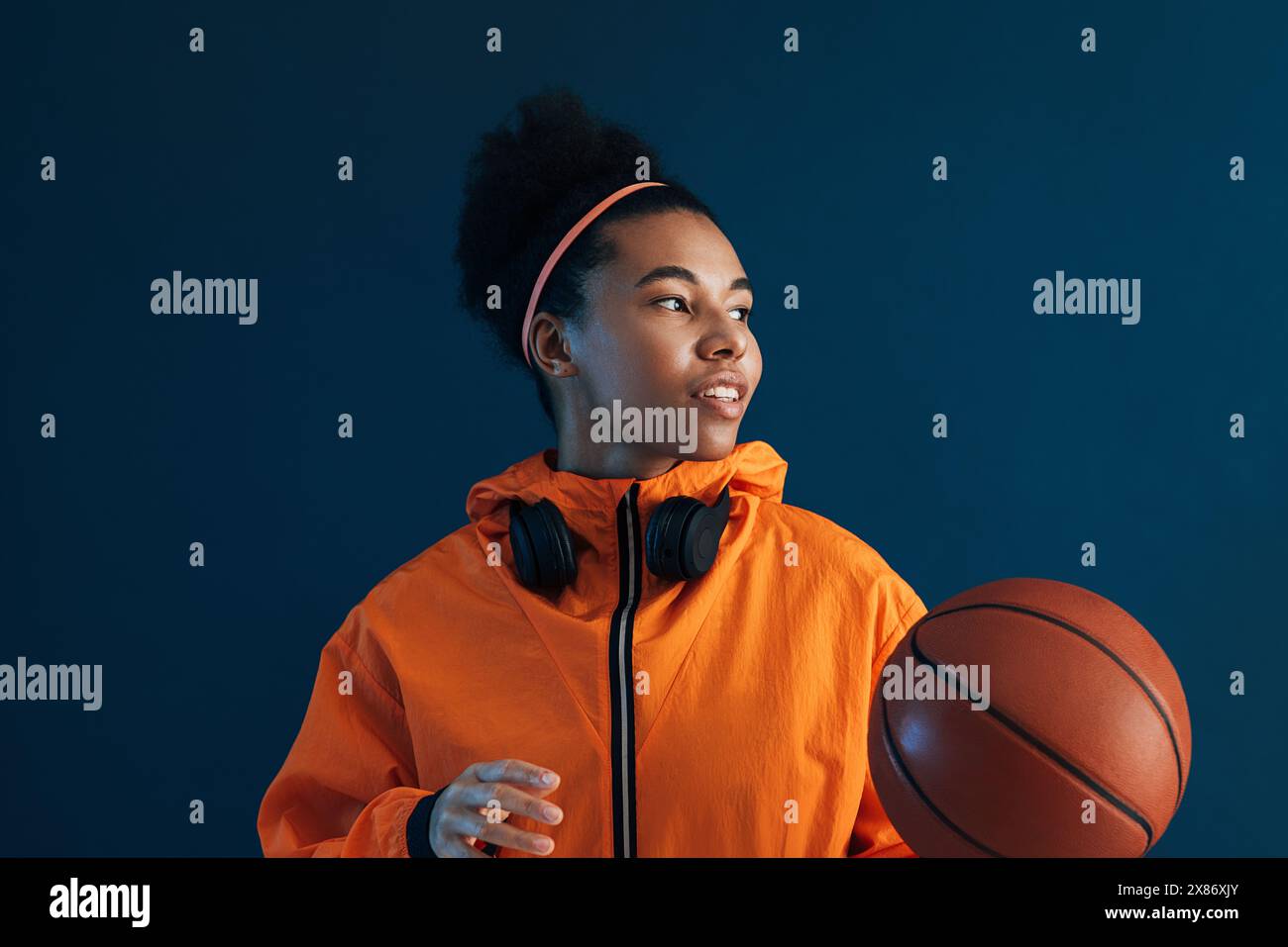 Ritratto di una giocatrice professionista di basket che guarda lontano in uno studio. Giocatrice di basket sicura di sé che indossa un abbigliamento sportivo arancione. Foto Stock