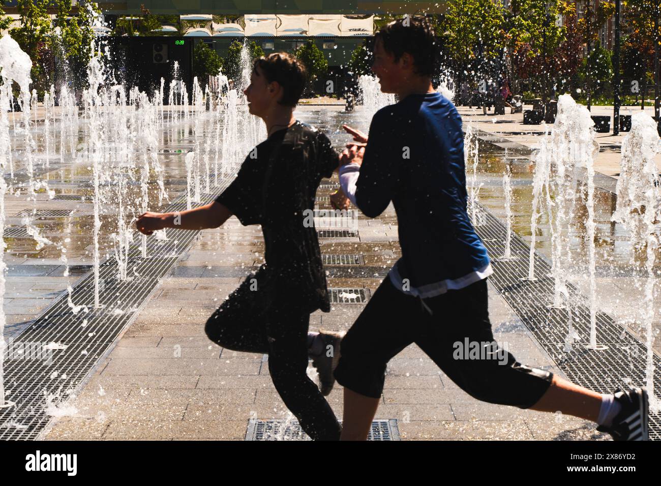 Mosca, Russia - 23 maggio 2024: Due ragazzi adolescenti saltano sui getti di una fontana. Parco cittadino con una fontana in città. Freschezza in una giornata calda. Q. Alta Foto Stock