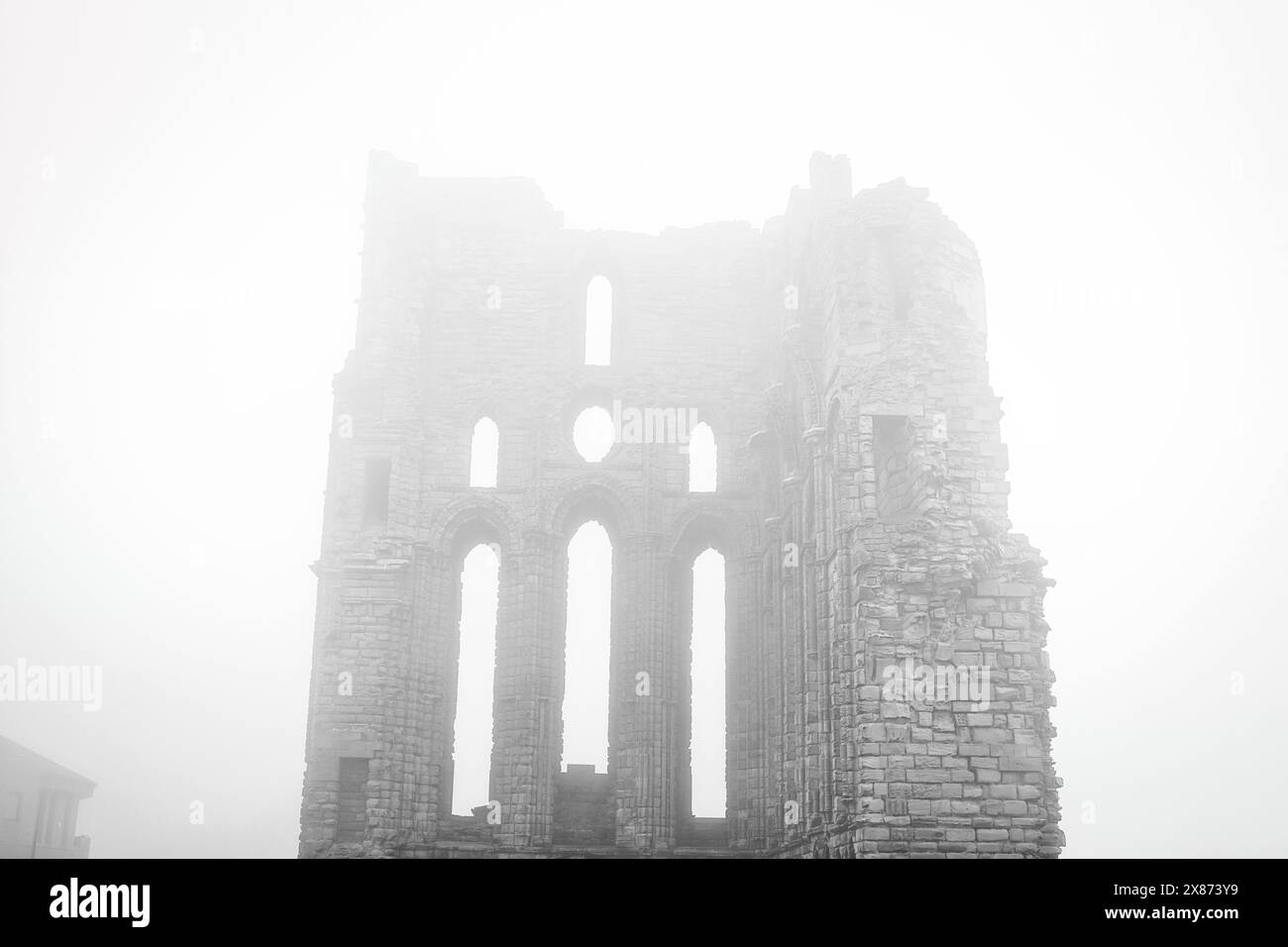 Una scena nebbiosa con le rovine di un antico edificio in pietra con alte finestre strette e archi. La struttura sembra essere parzialmente compressa, Foto Stock