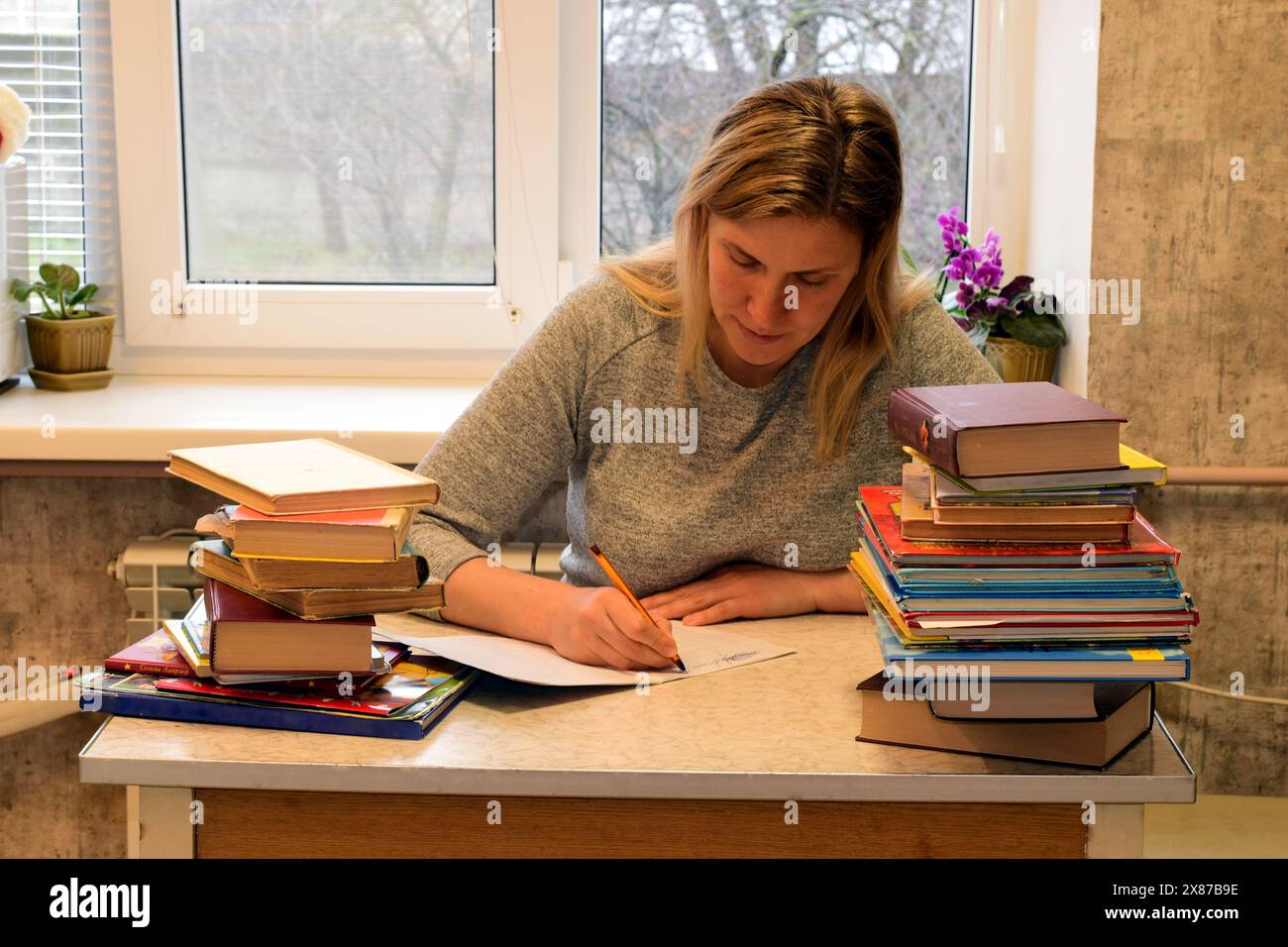 Seduta a un tavolo vicino alla finestra, una donna nota qualcosa con una penna stilografica in un taccuino. Foto di alta qualità Foto Stock