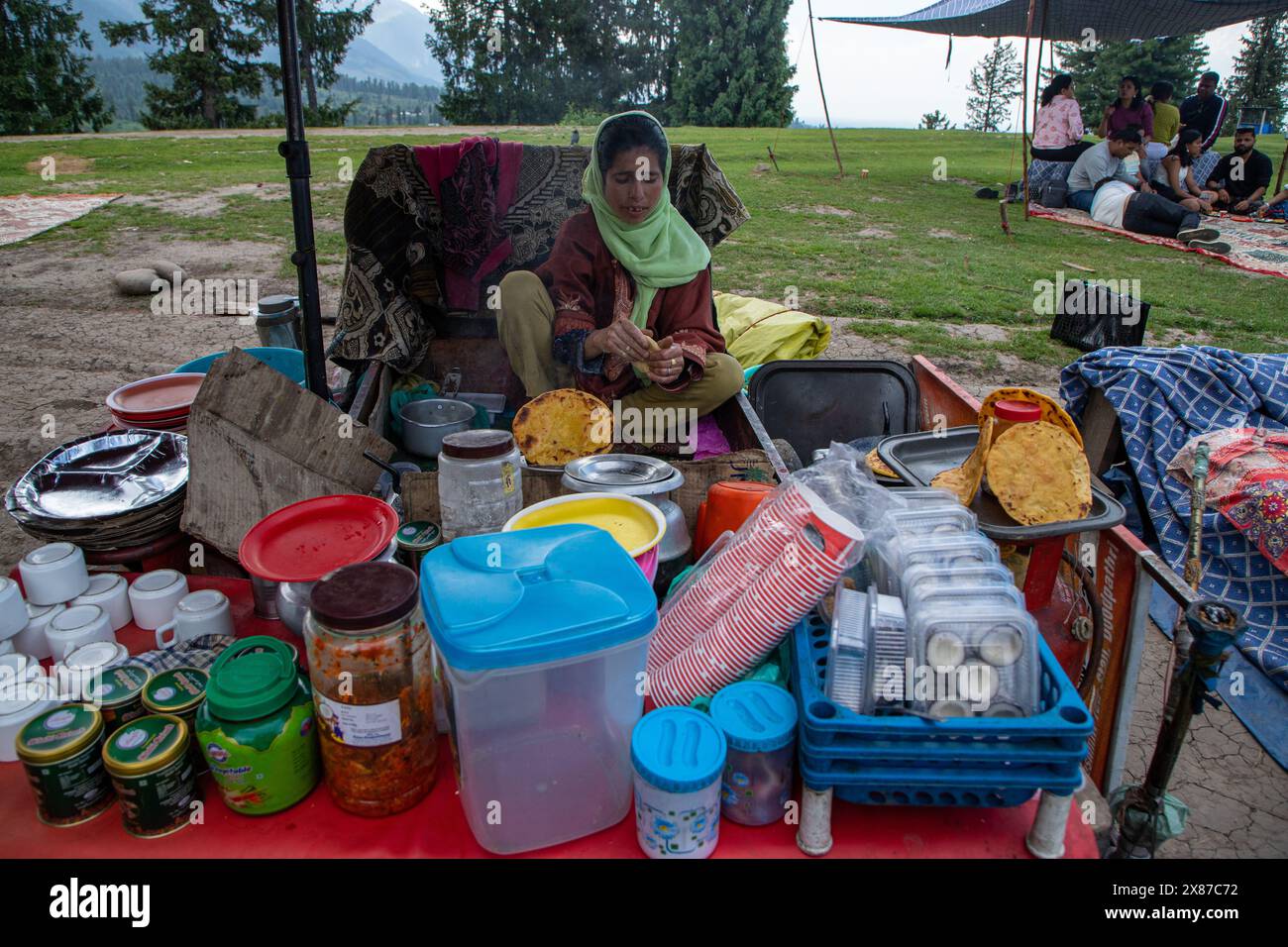 Una donna del Kashmir prepara tortillas di farina di mais mentre vende il Noon Chai (tè salato) ai turisti e alla gente del posto passando per il suo chiosco lungo la strada Doodhpathri nel distretto di Budgam, a sud-ovest di Srinagar. Le autorità hanno chiesto ai proprietari dei venditori di tè di liberare lo spazio che hanno occupato "illegalmente" entro dieci giorni o di affrontare azioni. I funzionari hanno detto a un'agenzia di stampa locale che l'autorità per lo sviluppo del turismo ha ricevuto molte lamentele per il fatto che i proprietari delle bancarelle di tè hanno tagliato rami di alberi, danneggiando così i pittoreschi prati. Sulla strada per i prati del famoso To Foto Stock