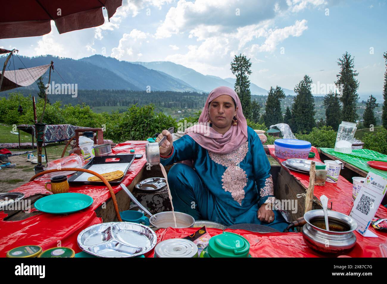 Una donna del Kashmir prepara il Noon Chai (tè salato) e lo serve con tortillas di farina di mais ai turisti e alla gente del posto passando per il suo chiosco lungo la strada Doodhpathri nel distretto di Budgam, a sud-ovest di Srinagar. Le autorità hanno chiesto ai proprietari dei venditori di tè di liberare lo spazio che hanno occupato "illegalmente" entro dieci giorni o di affrontare azioni. I funzionari hanno detto a un'agenzia di stampa locale che l'autorità per lo sviluppo del turismo ha ricevuto molte lamentele per il fatto che i proprietari delle bancarelle di tè hanno tagliato rami di alberi, danneggiando così i pittoreschi prati. Sulla strada per i prati della fam Foto Stock