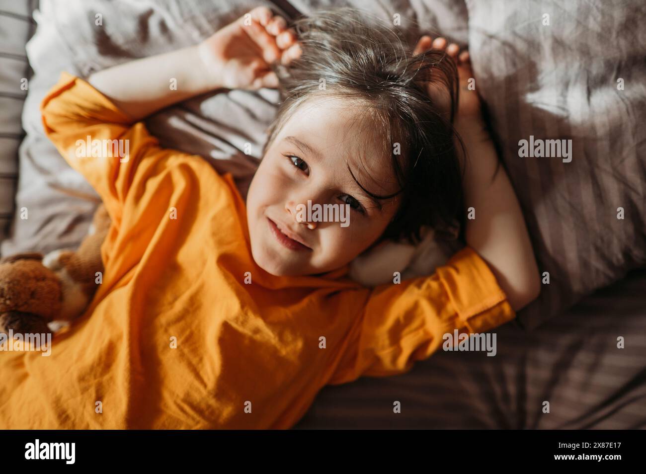 Ritratto di un ragazzo carino con i capelli lunghi sdraiato sul letto con una felpa arancione a casa Foto Stock