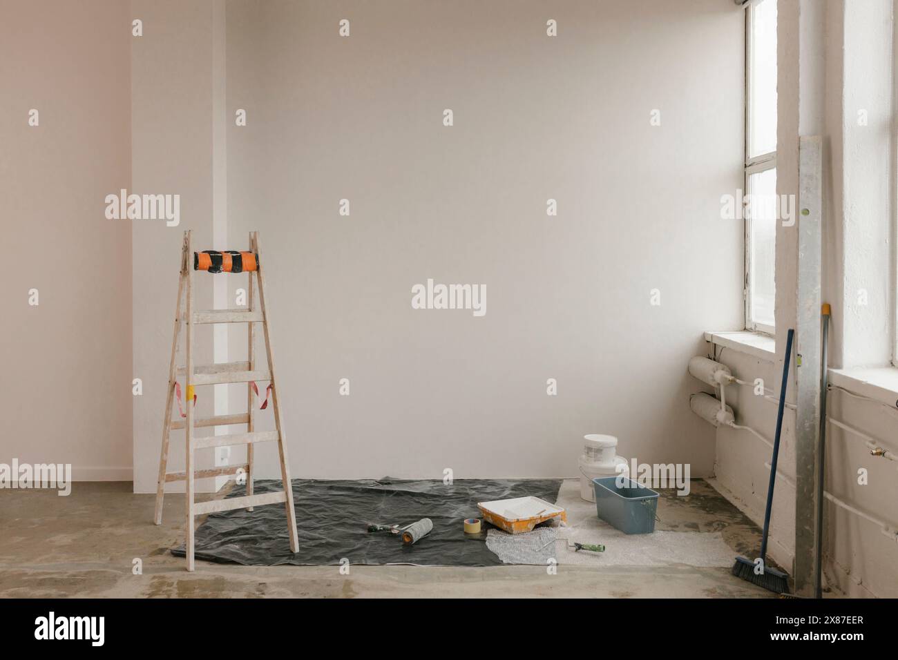 Scala accanto all'attrezzatura di verniciatura vicino alla parete bianca di casa Foto Stock