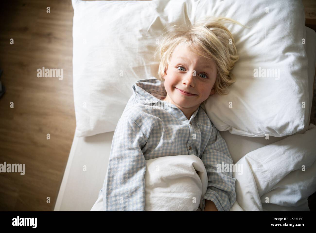 Ragazzo sorridente che indossa pigiami e si sdraia sul letto a casa Foto Stock