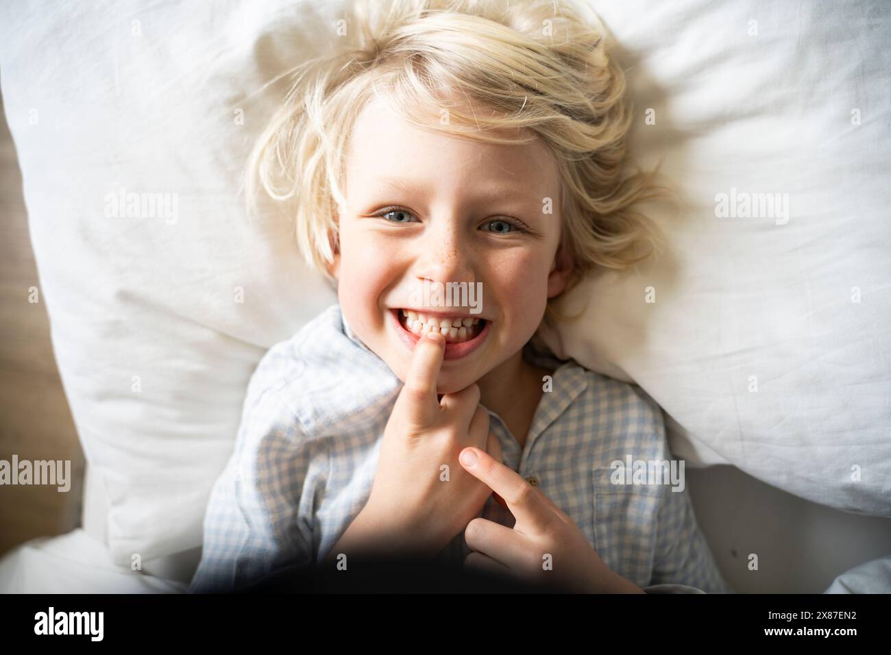 Ragazzo felice che tocca e mostra i denti sul letto a casa Foto Stock