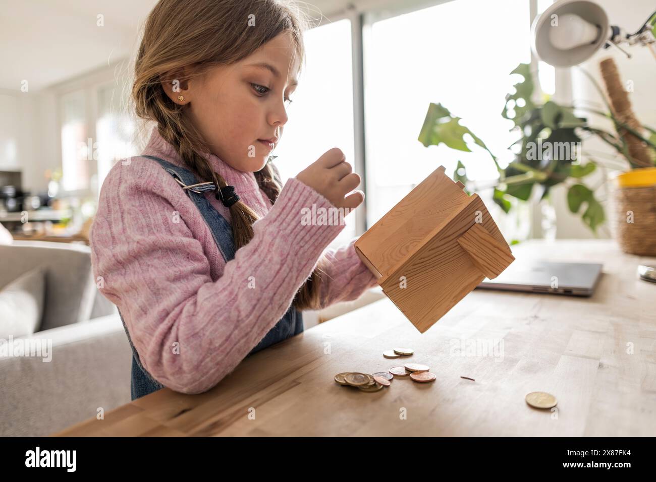 Ragazza con un banco di monete di legno a tavola a casa Foto Stock
