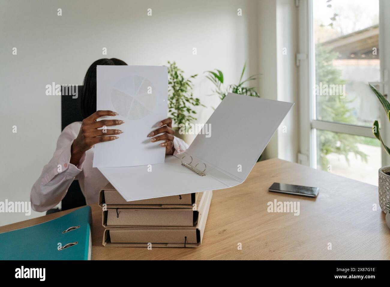 Donna che deposita documenti in una cartella alla scrivania in ufficio Foto Stock