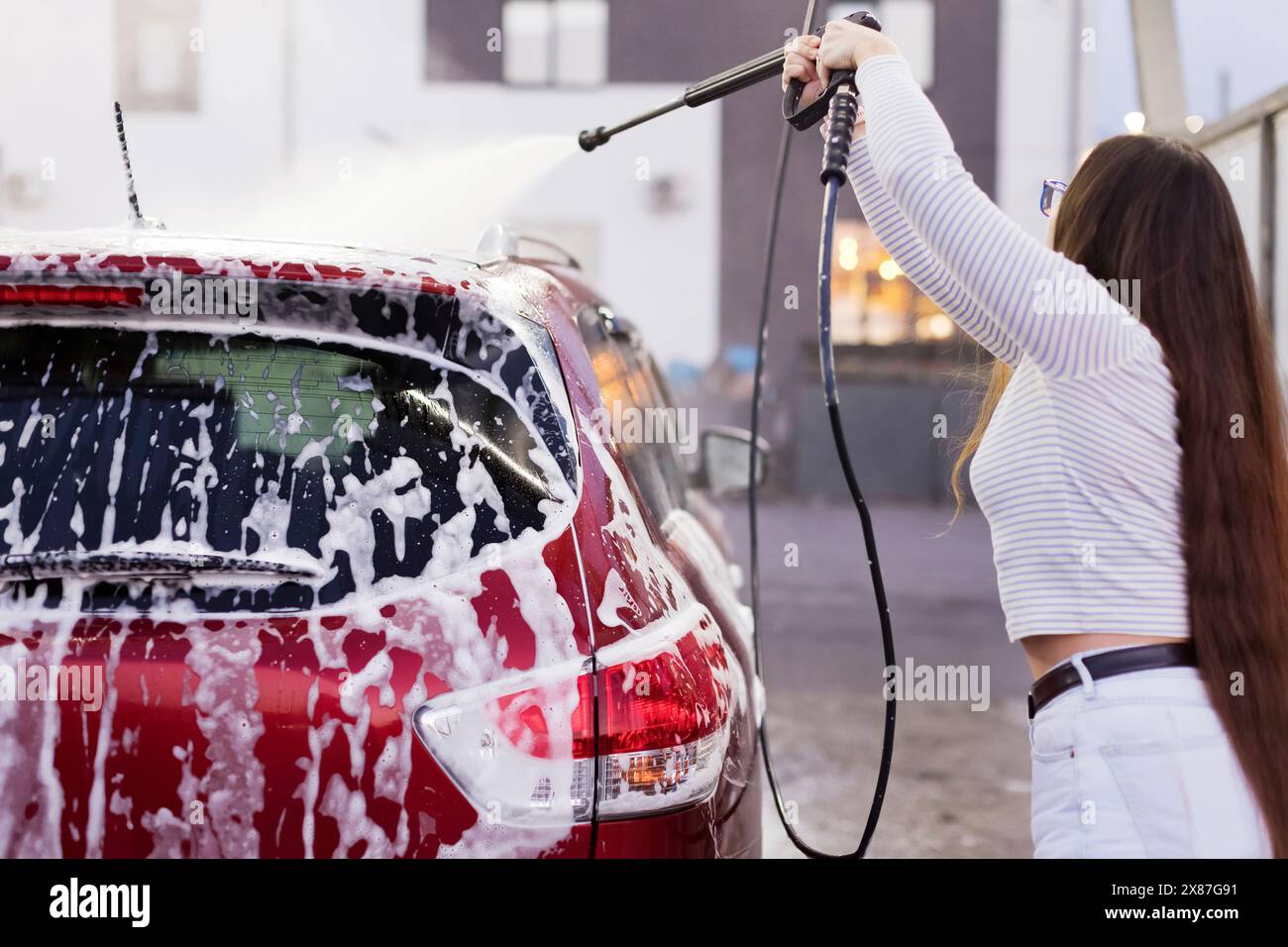 Donna che pulisce l'auto con acqua ad alta pressione in garage Foto Stock
