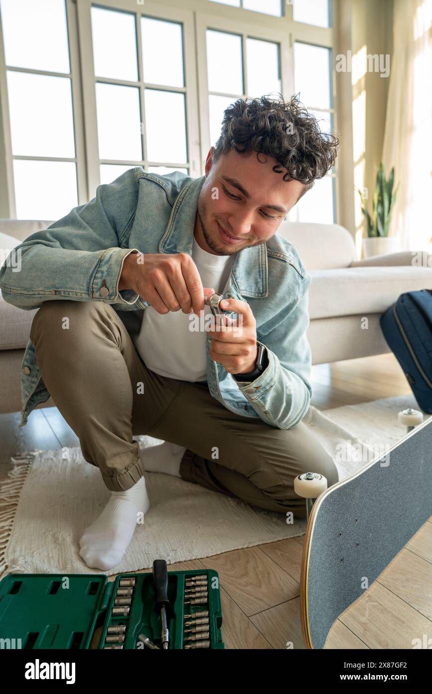 Un giovane sorridente seduto con la cassetta degli attrezzi vicino allo skateboard a casa Foto Stock