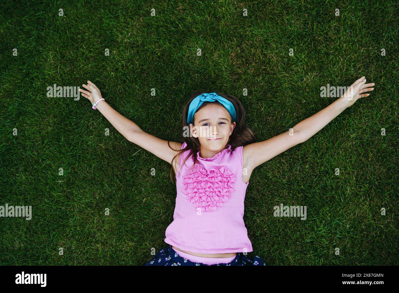 Ragazza sorridente con le braccia allungate distese sull'erba Foto Stock