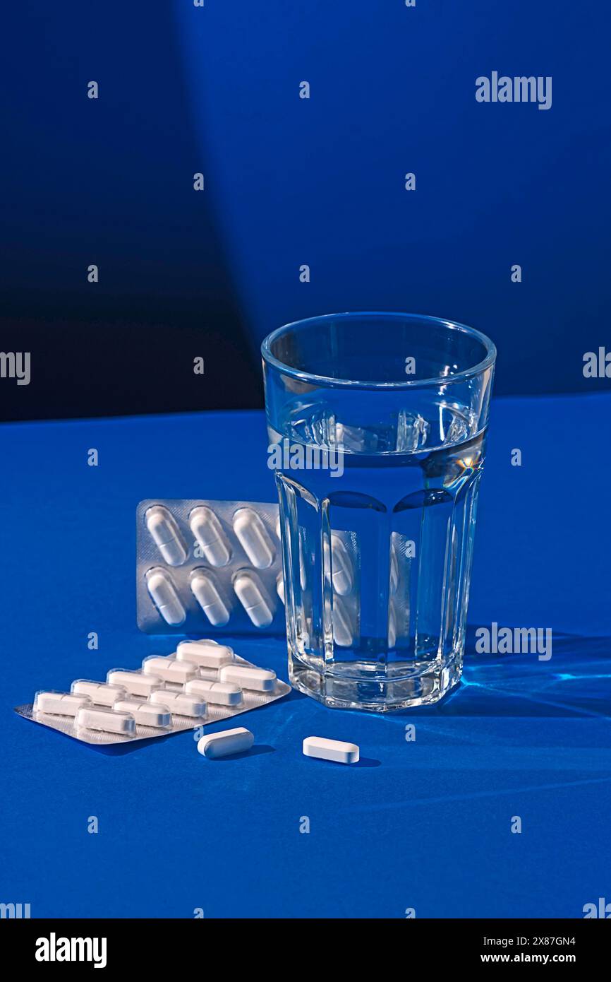 Pillole e bicchiere di acqua su sfondo blu Foto Stock
