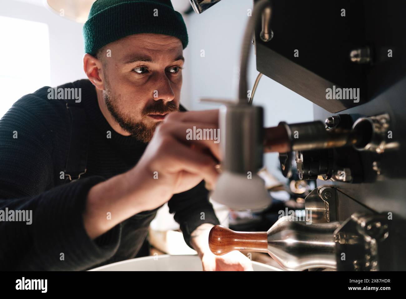 Torrefazione del caffè con cappello in maglia e macchinari in funzione in fabbrica Foto Stock