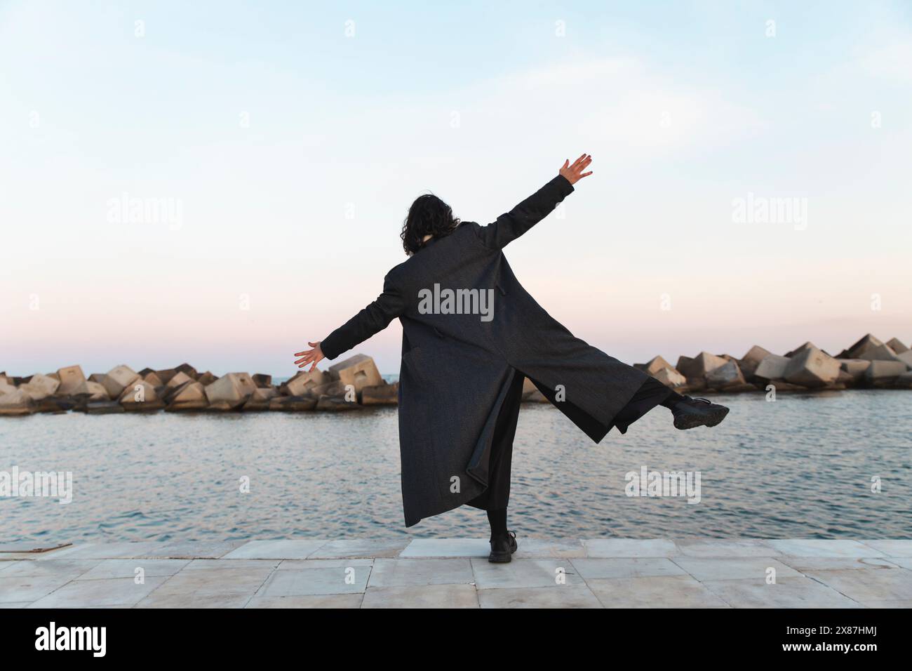 Giovane donna con le braccia tese in equilibrio su una gamba vicino al mare Foto Stock