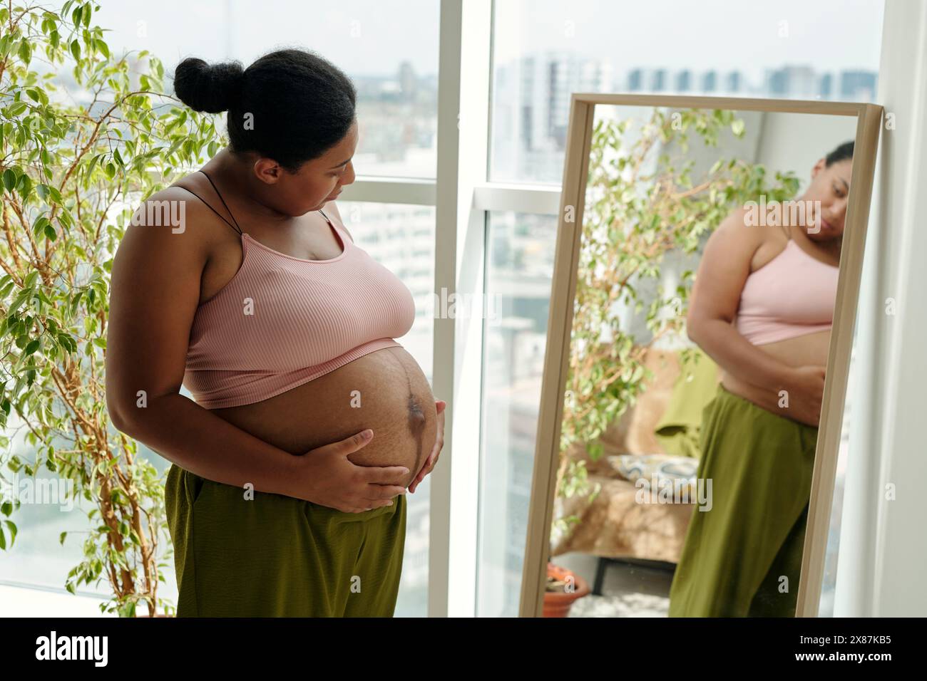 Donna incinta di dimensioni più grandi con mani sullo stomaco che guarda il riflesso specchio Foto Stock