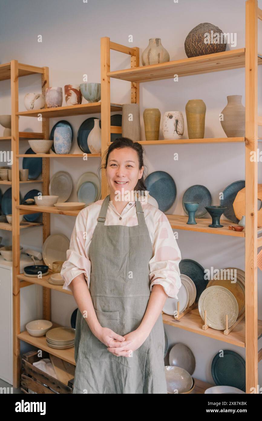 Artigiani sorridenti in piedi a scaffale con ceramiche in studio d'arte Foto Stock
