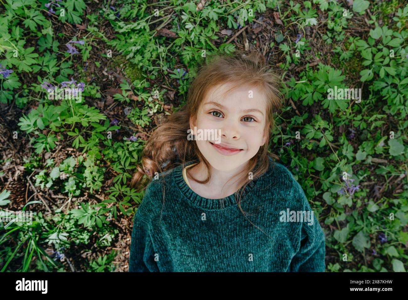 Ragazza sorridente sdraiata sull'erba nella foresta Foto Stock