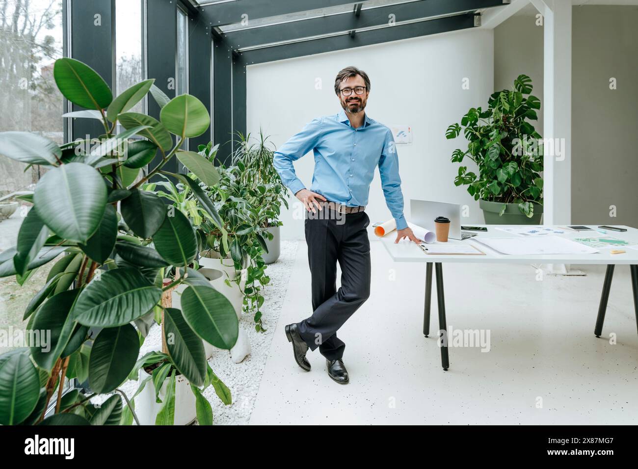 Un uomo d'affari sorridente in piedi vicino alle piante in ufficio Foto Stock