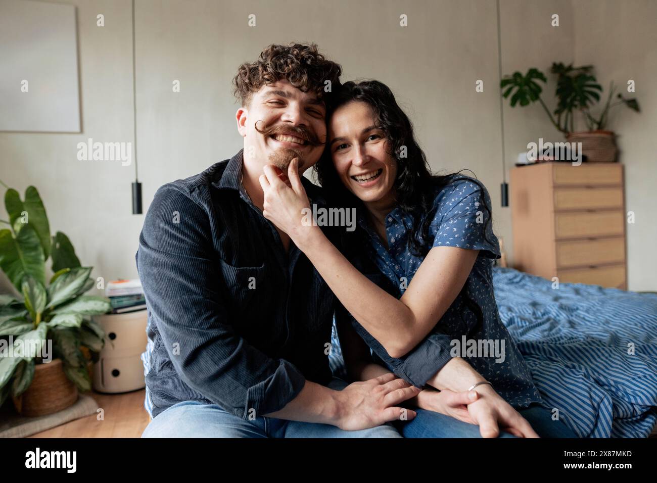 Donna sorridente che tocca il mento del fidanzato seduto sul letto a casa Foto Stock