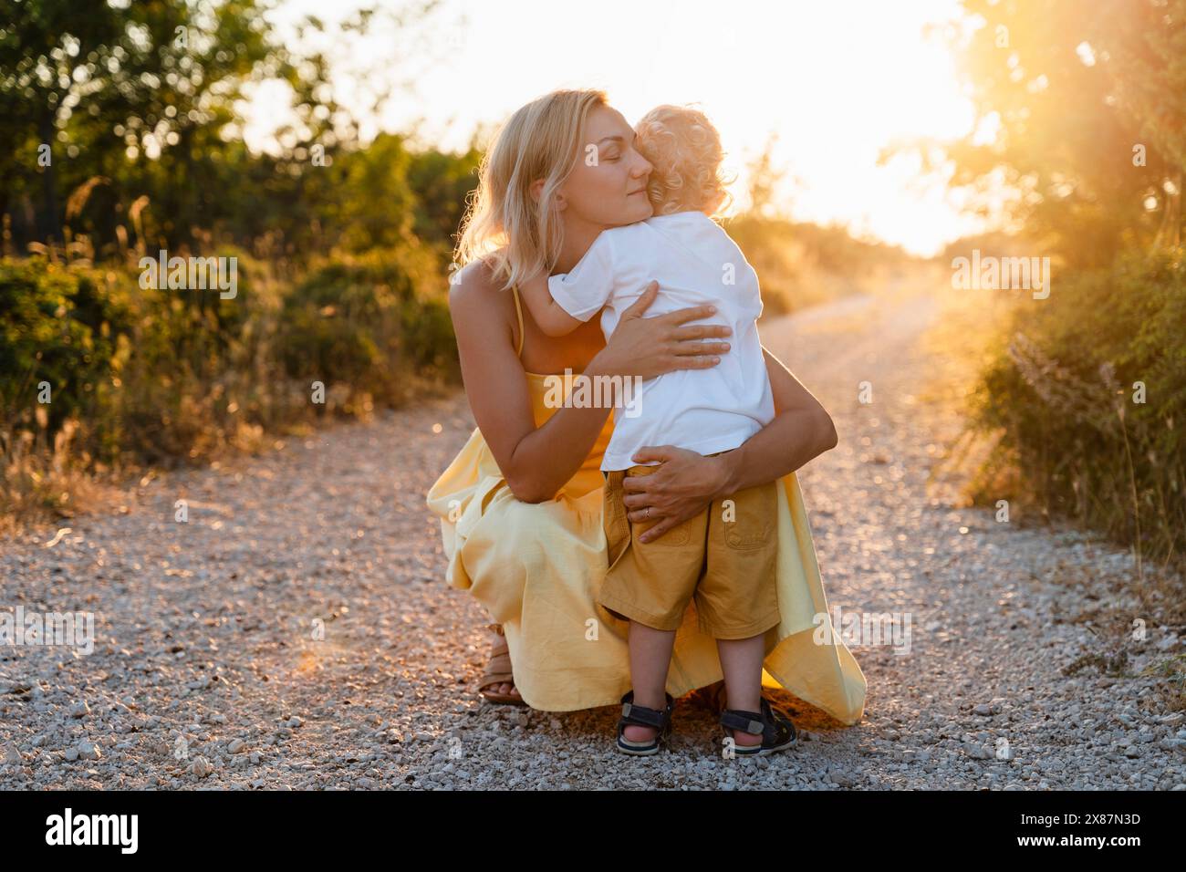 Madre che abbraccia il figlio sul sentiero al tramonto Foto Stock