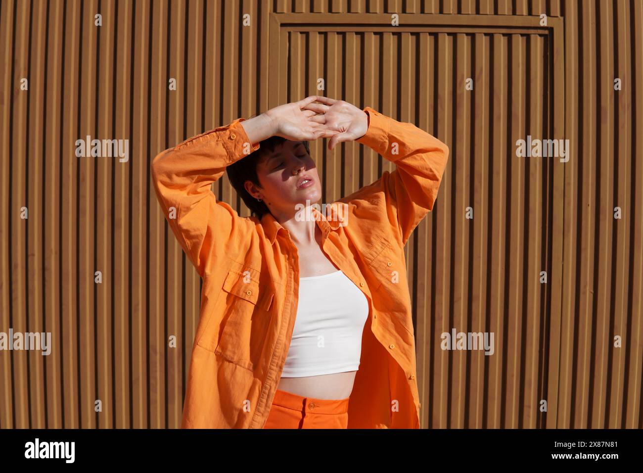 Donna che protegge gli occhi chiusi con le mani in piedi davanti alla parete marrone Foto Stock
