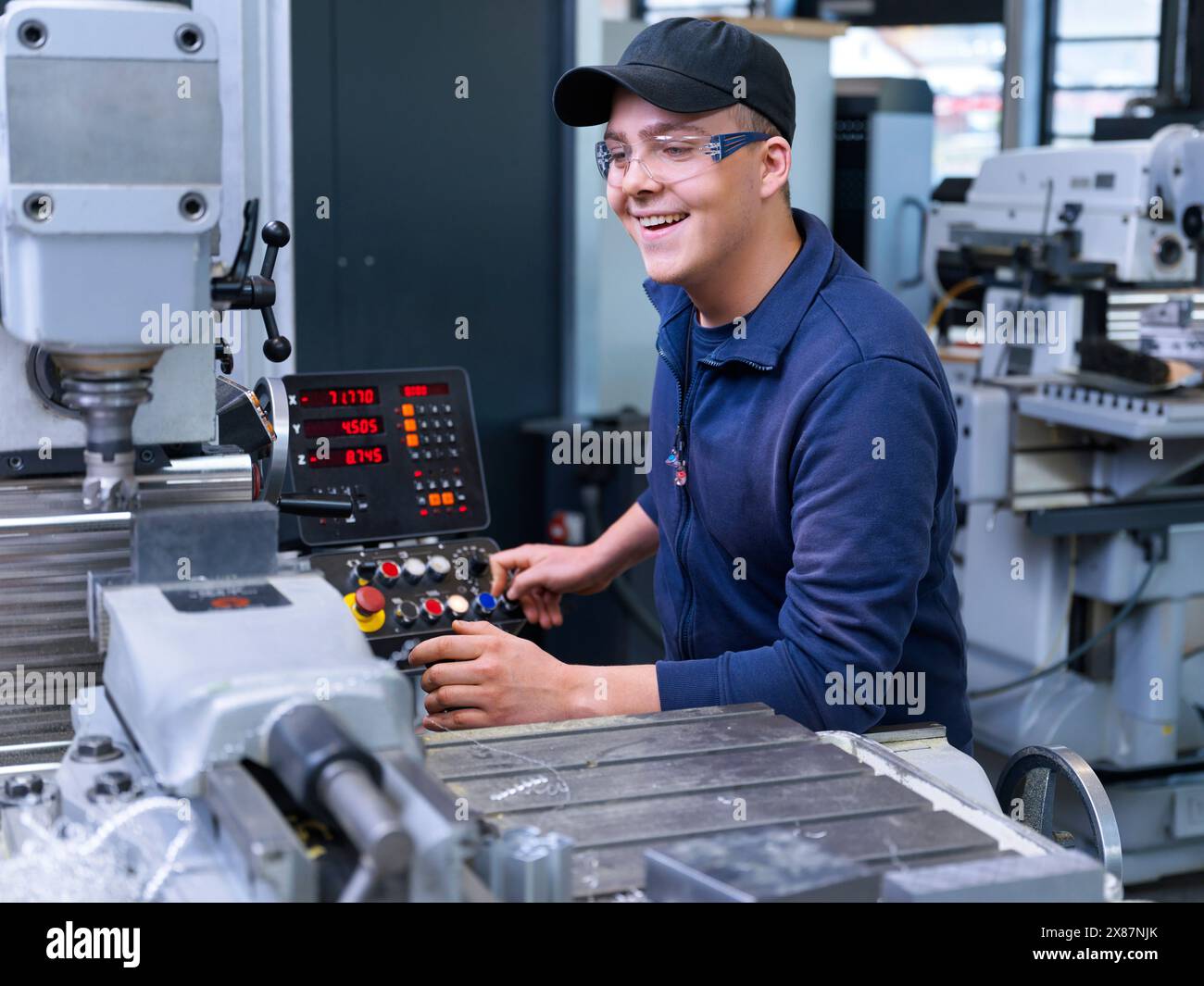 Felice apprendista che lavora con macchine CNC in fabbrica Foto Stock