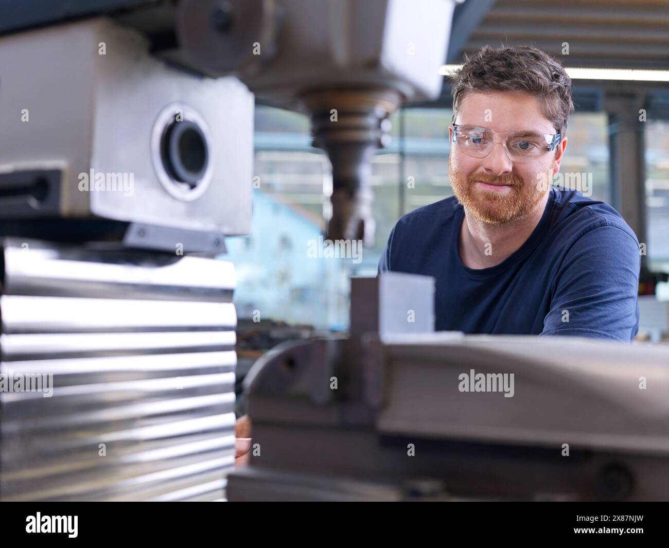 Tecnico che indossa occhiali protettivi che esamina la macchina CNC in fabbrica Foto Stock
