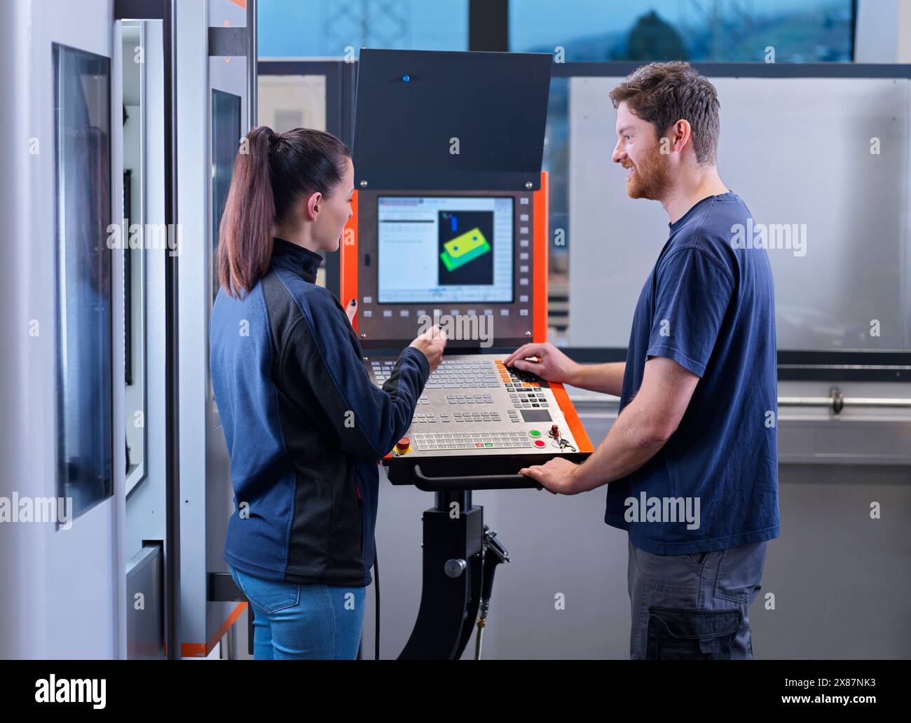 Lavoratori di fabbrica che parlano tra loro vicino a macchine CNC nell'industria Foto Stock