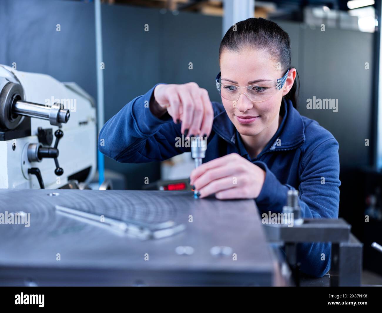 Tecnico che indossa occhiali di sicurezza e pezzi di misurazione in fabbrica Foto Stock