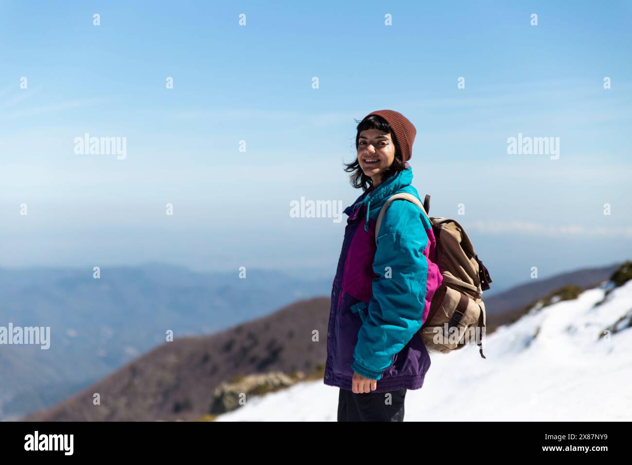 Donna sorridente con zaino in piedi su una montagna innevata Foto Stock