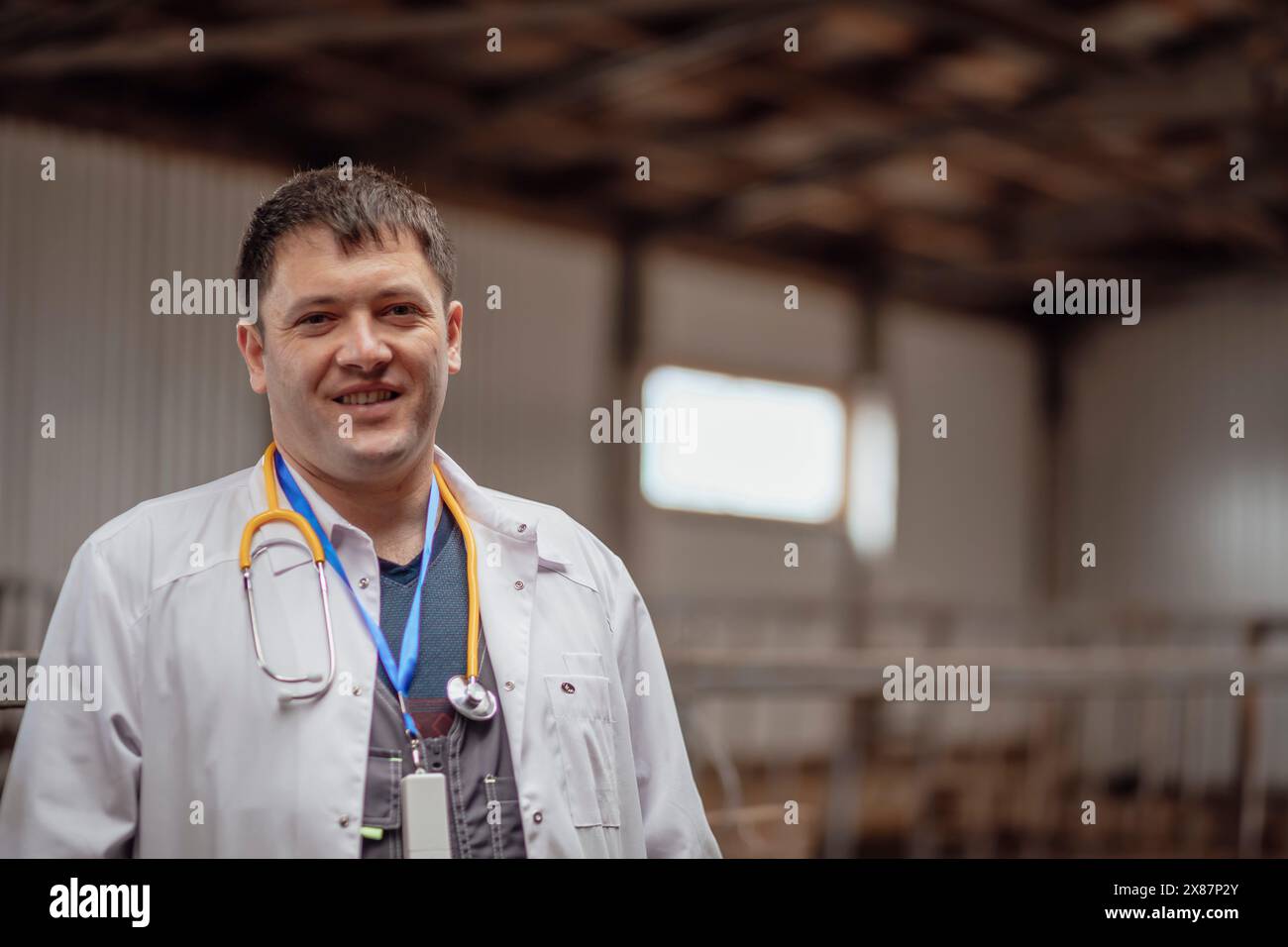 Veterinario sorridente che indossa un camice da laboratorio e si trova in piedi in fattoria Foto Stock