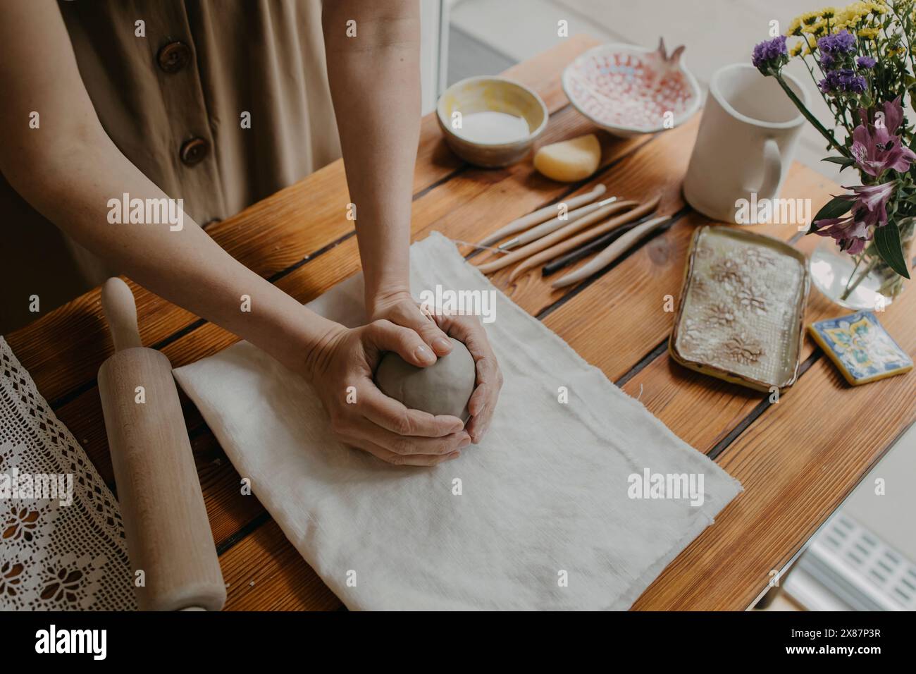 Mani di donna che tengono l'argilla su un panno bianco a casa Foto Stock