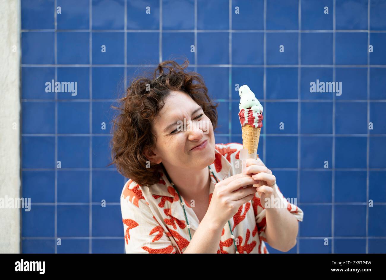 Donna allegra che tiene il cono del gelato davanti a una parete di piastrelle blu Foto Stock