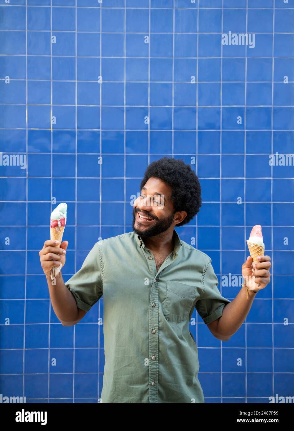 Giovane felice che tiene i coni del gelato davanti al muro blu Foto Stock