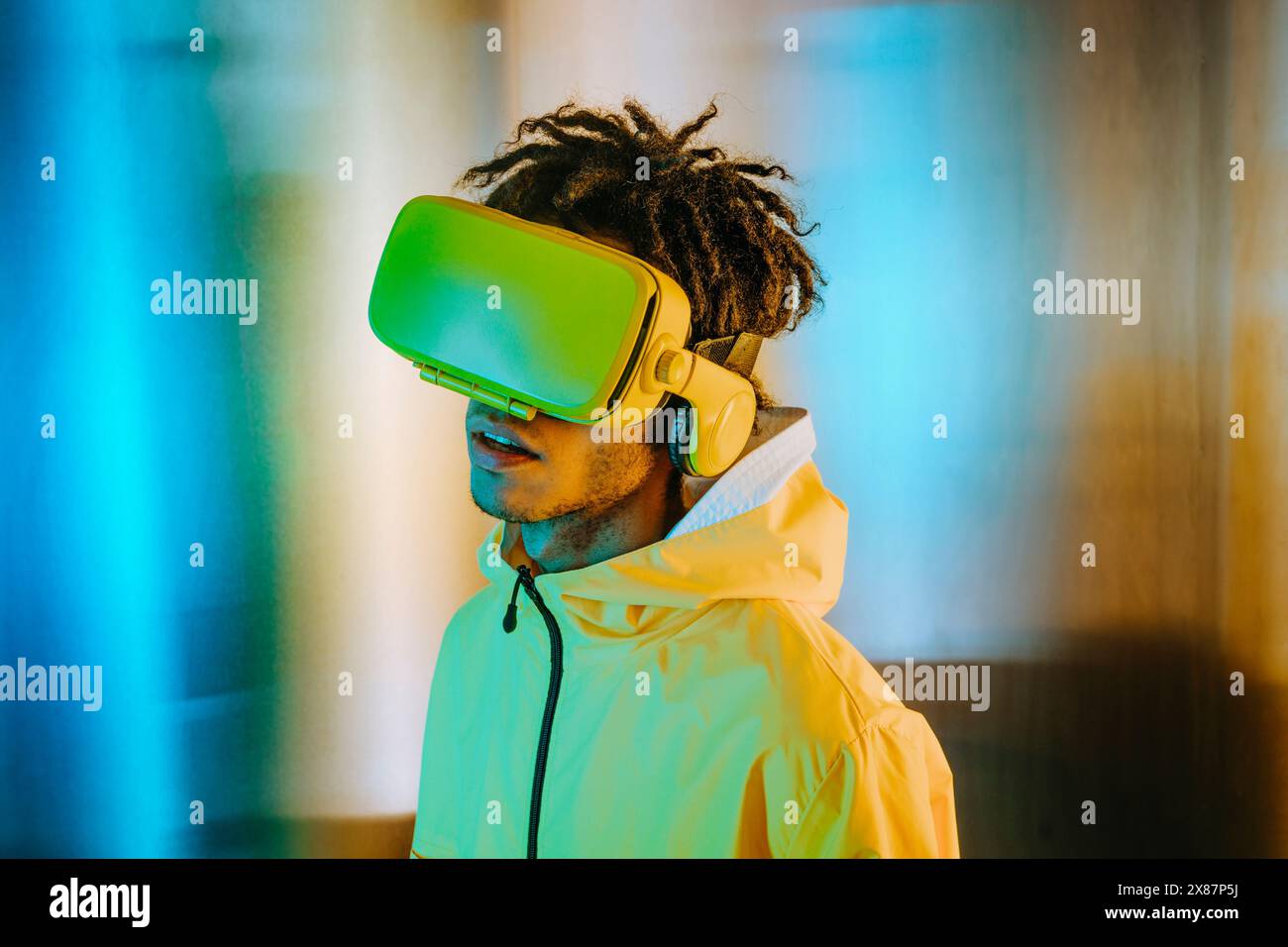 Uomo con paura che indossa un visore per la realtà virtuale vicino a una parete illuminata Foto Stock