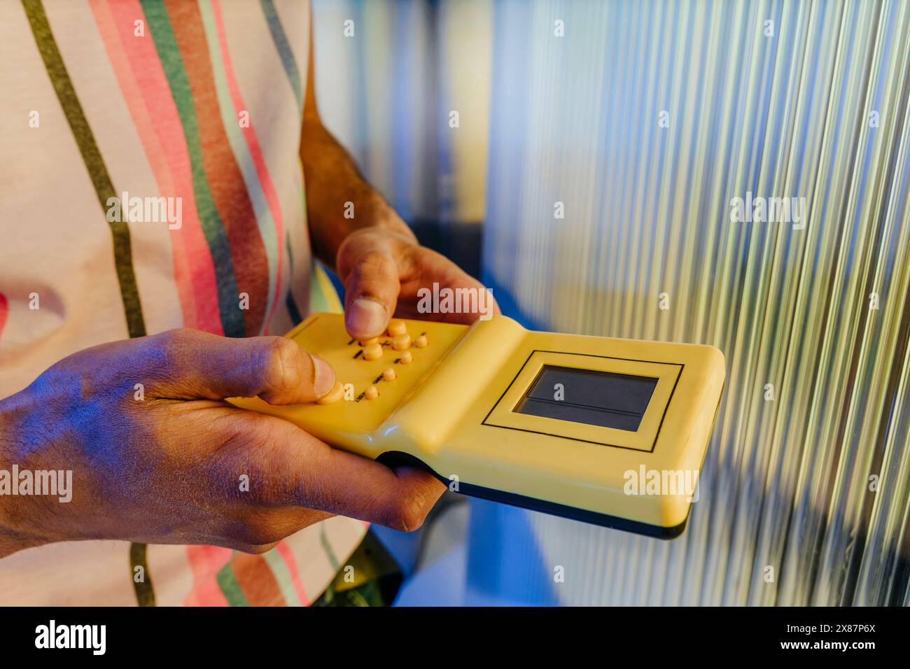 Uomo che gioca a un gioco portatile di colore giallo vicino a un muro a righe Foto Stock