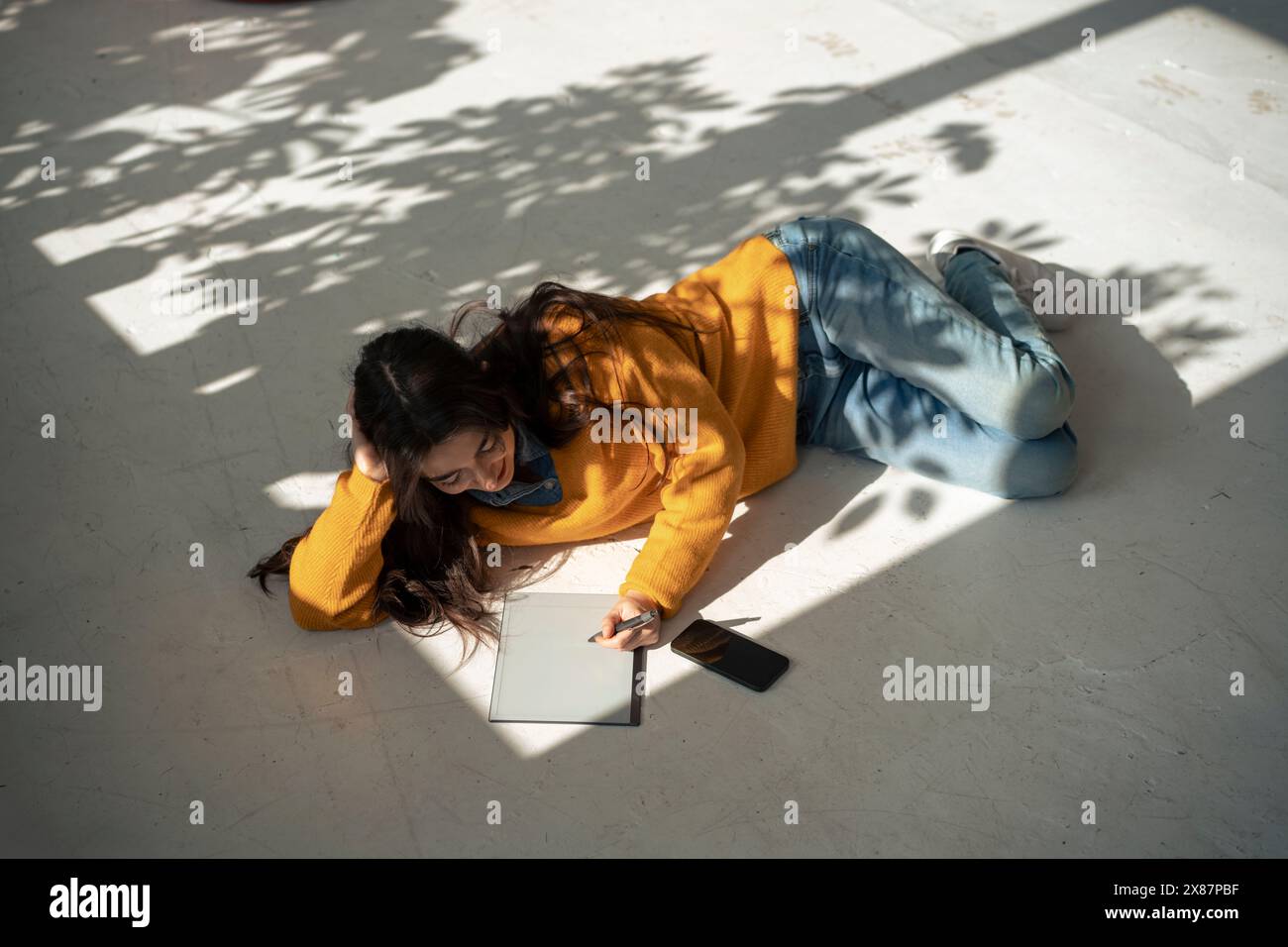 Giovane donna che utilizza un tablet PC sdraiata sul pavimento di casa Foto Stock